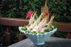 Un bol de nourriture avec des baguettes et des éléments décoratifs, posé sur une table avec une rambarde en bois en arrière-plan.