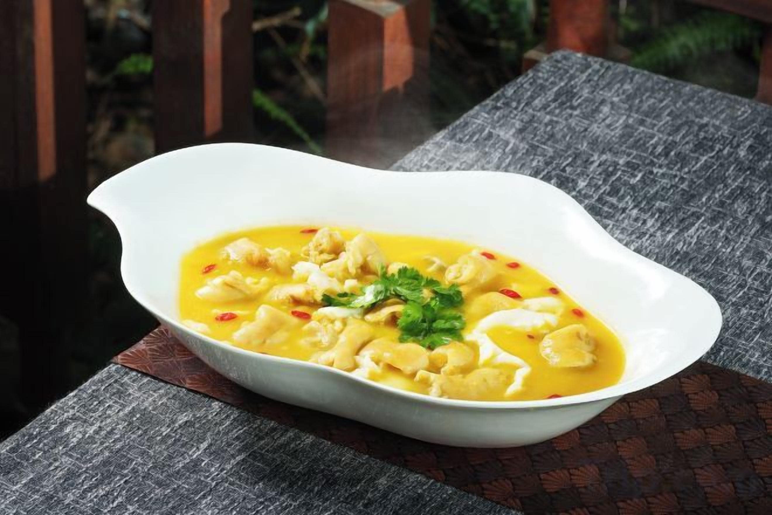 A white bowl of soup on a wooden table with a woven tablecloth.
