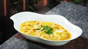 A white bowl of soup on a wooden table with a woven tablecloth.