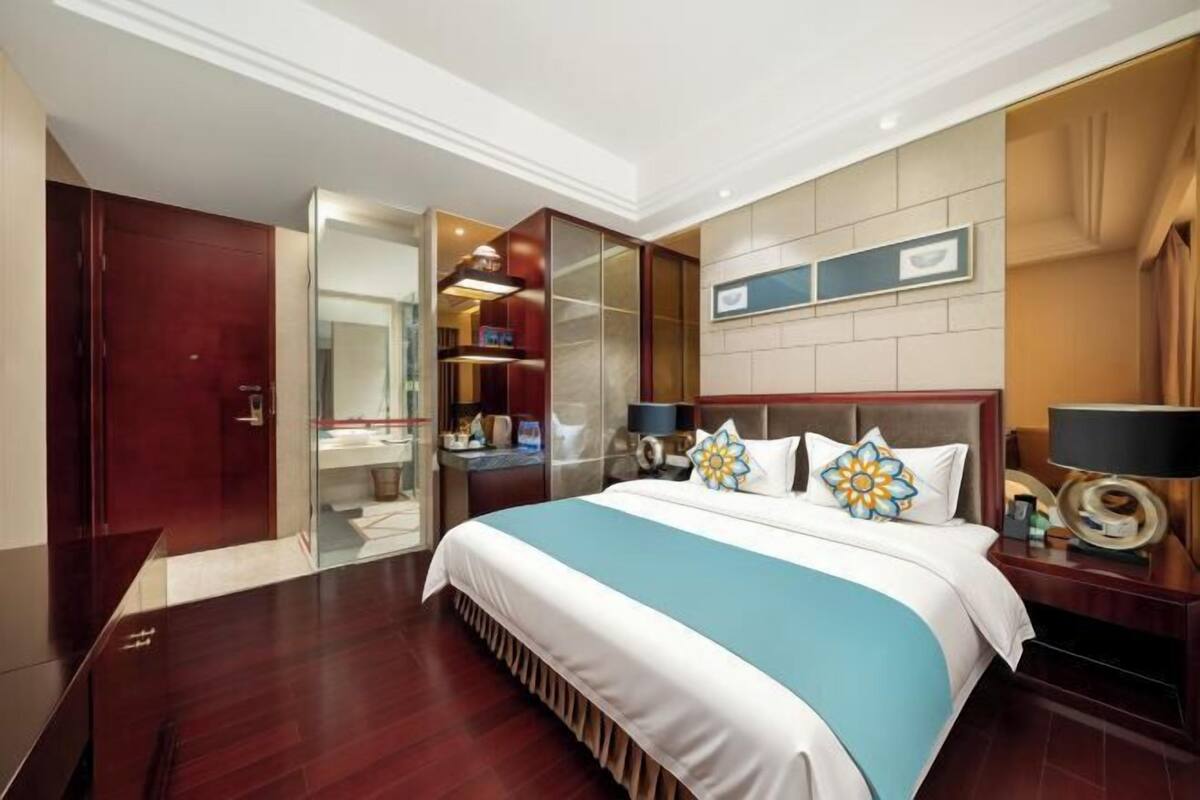 A hotel room with a large bed, a wardrobe, a bathroom, and a desk with a lamp.