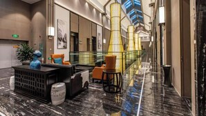 Un hall d’hôtel moderne avec un sol en marbre, des espaces de détente et une balustrade en verre donnant sur l’intérieur.