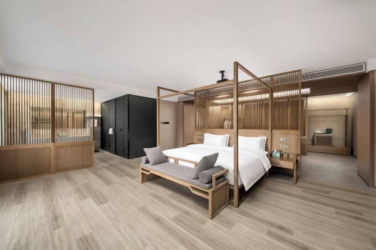 A modern bedroom with a wooden bed frame, a bench, and a separate sleeping area with a desk and chair.