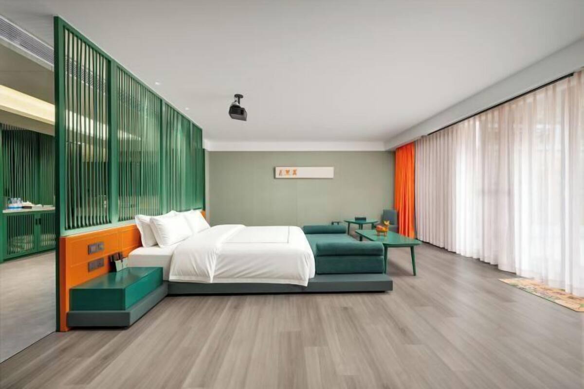 A modern bedroom with a bed, a desk, and a green partition.