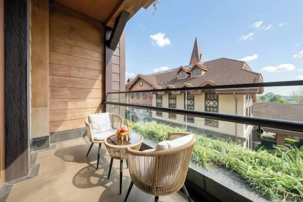 A balcony with wicker chairs and a small table, overlooking a building with a pointed roof and a visible window.