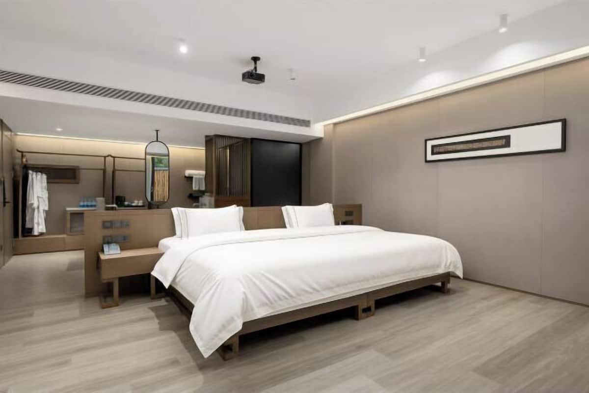 A modern bedroom with a large bed, a vanity with a mirror, and a wall-mounted artwork.
