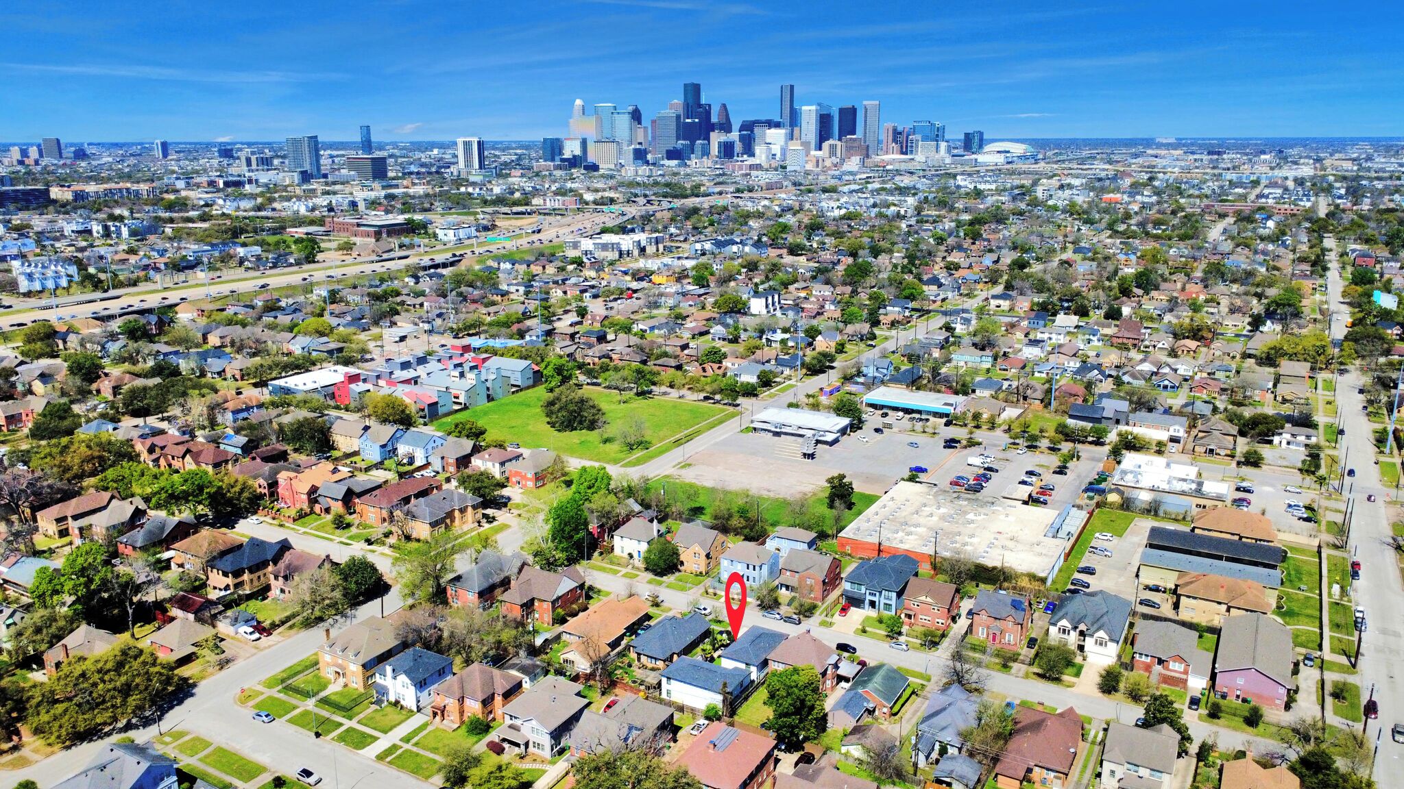 An aerial view of a residential area with houses, a parking lot, and a distant city skyline.