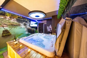 A hot tub in a room with a waterfall backdrop, a television, and a wooden table with candles. - Private spa Charleroi city center 8 minutes from the airport (Charleroi)