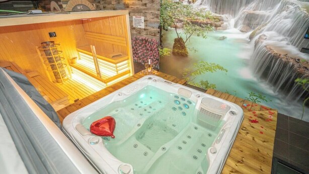 Een bubbelbad met een watervalreliëf, een houten sauna en een toilet.