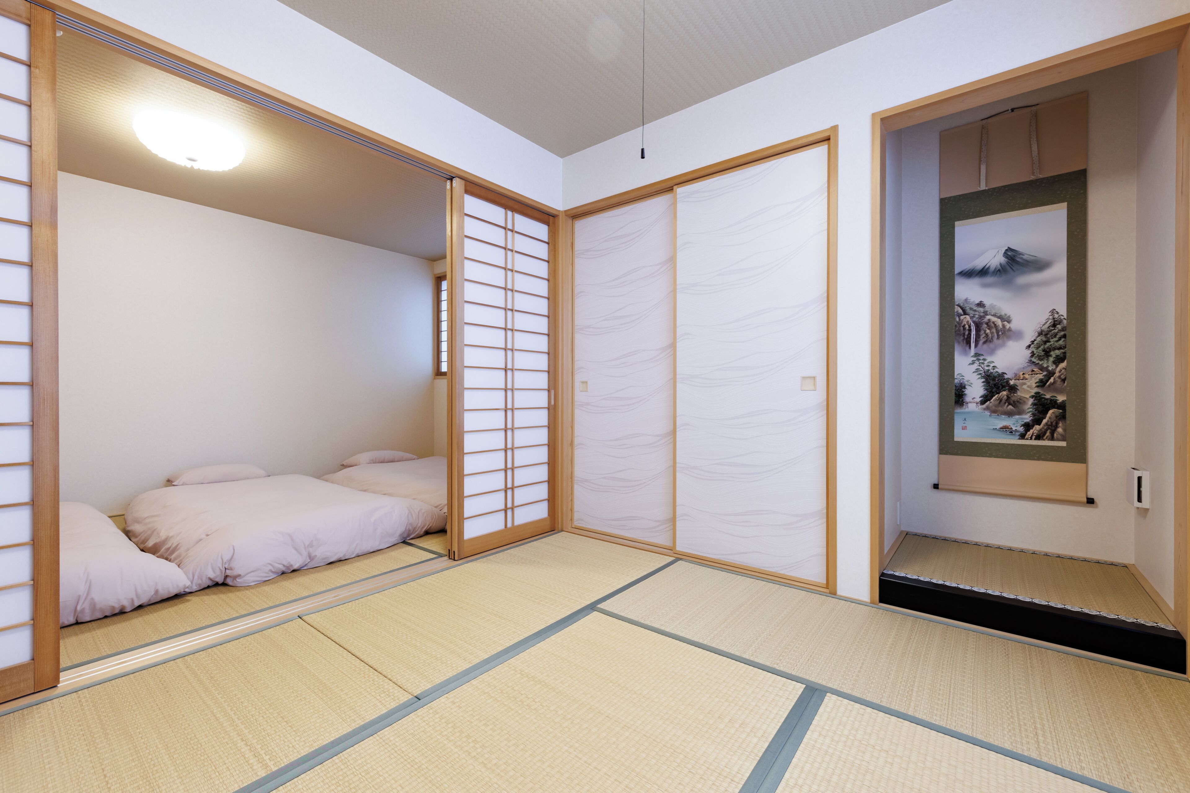 Een traditionele Japanse kamer met tatami vloeren, een futonbed, schuifdeuren en een lijstwerk met kunst.