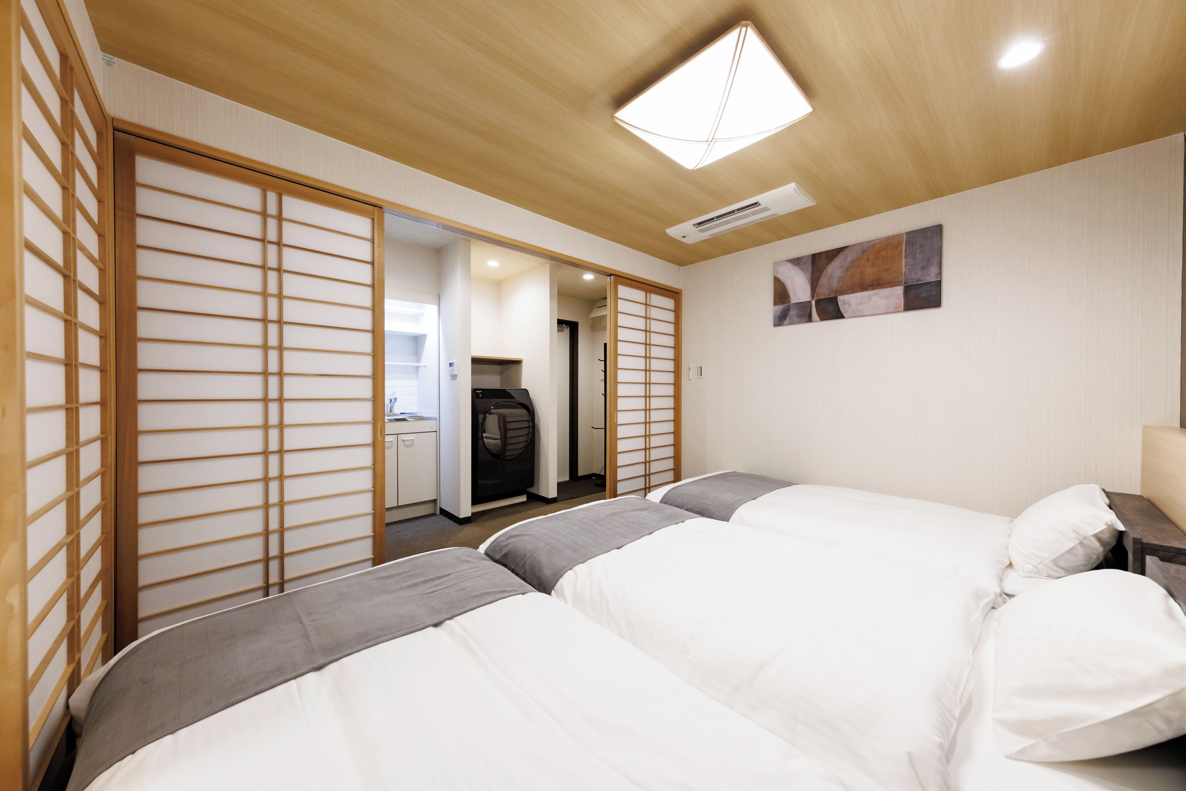 A hotel room with two beds, a sliding shoji screen, a ceiling fan, and a painting on the wall.