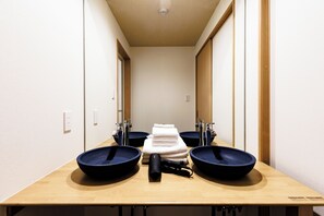 Ein Badezimmer mit drei Waschbecken, einem Stapel Handtücher und einem Fön.