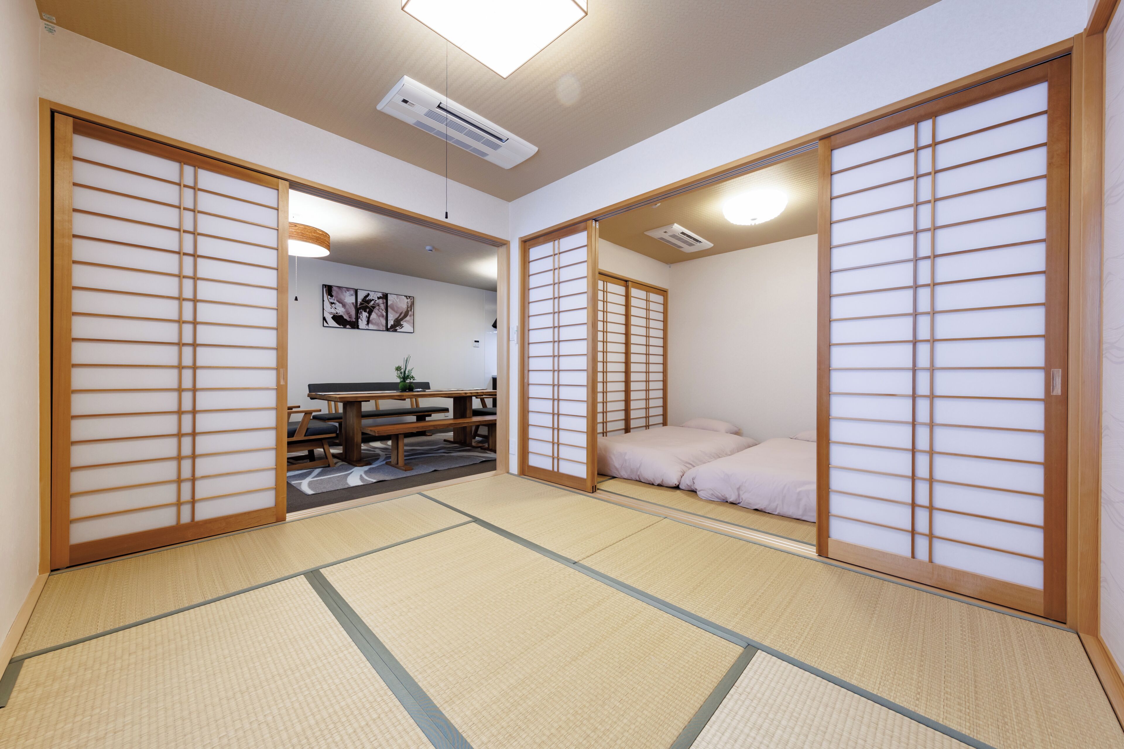 A traditional Japanese room with tatami flooring, sliding doors, a bed, and a table with chairs.