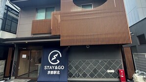 Een gebouw met een moderne gevel, een bord waarop 'STAY&GO' staat en een parkeerplaats ervoor.