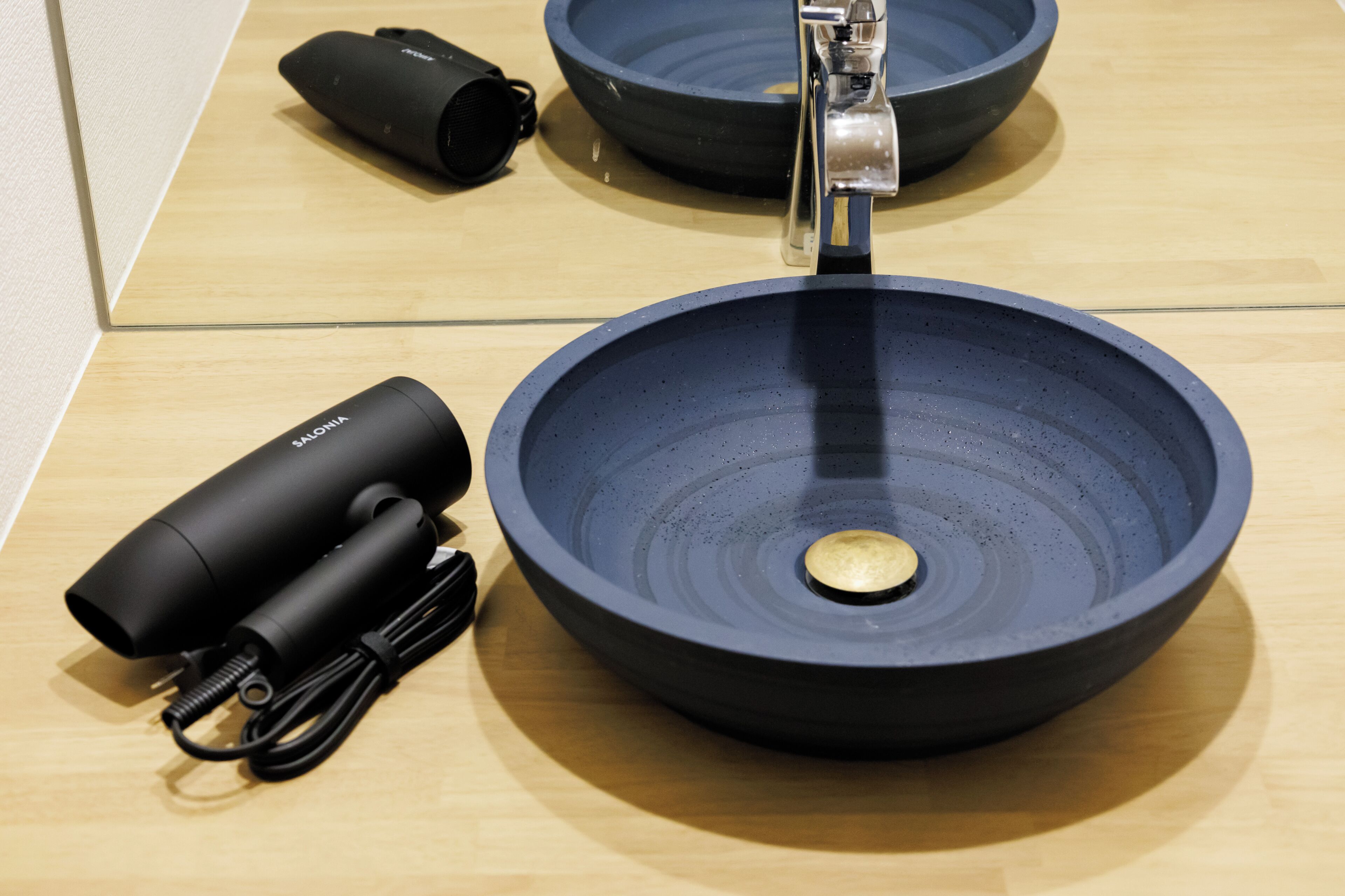 A modern bathroom with a large, dark blue sink, a faucet, and a black handheld device.