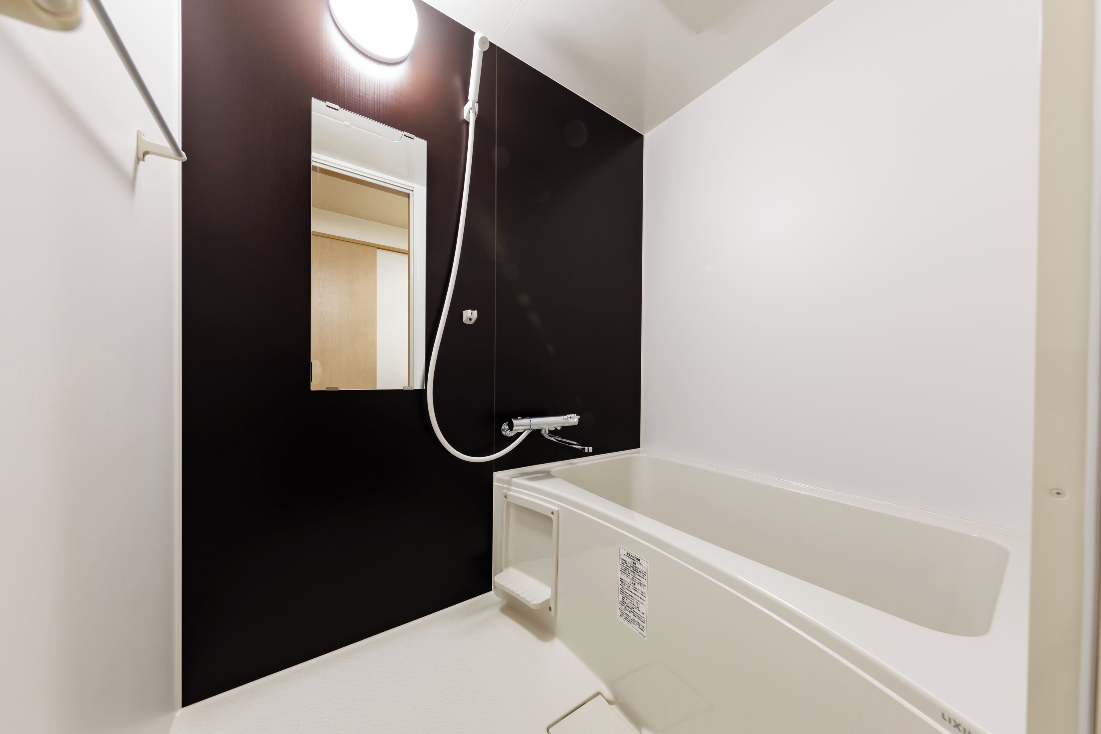 A bathroom with a white bathtub, a black wall, and a mirror.
