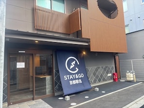 Entrada de un hotel con un cartel azul que muestra 'STAY&GO' y caracteres japoneses.