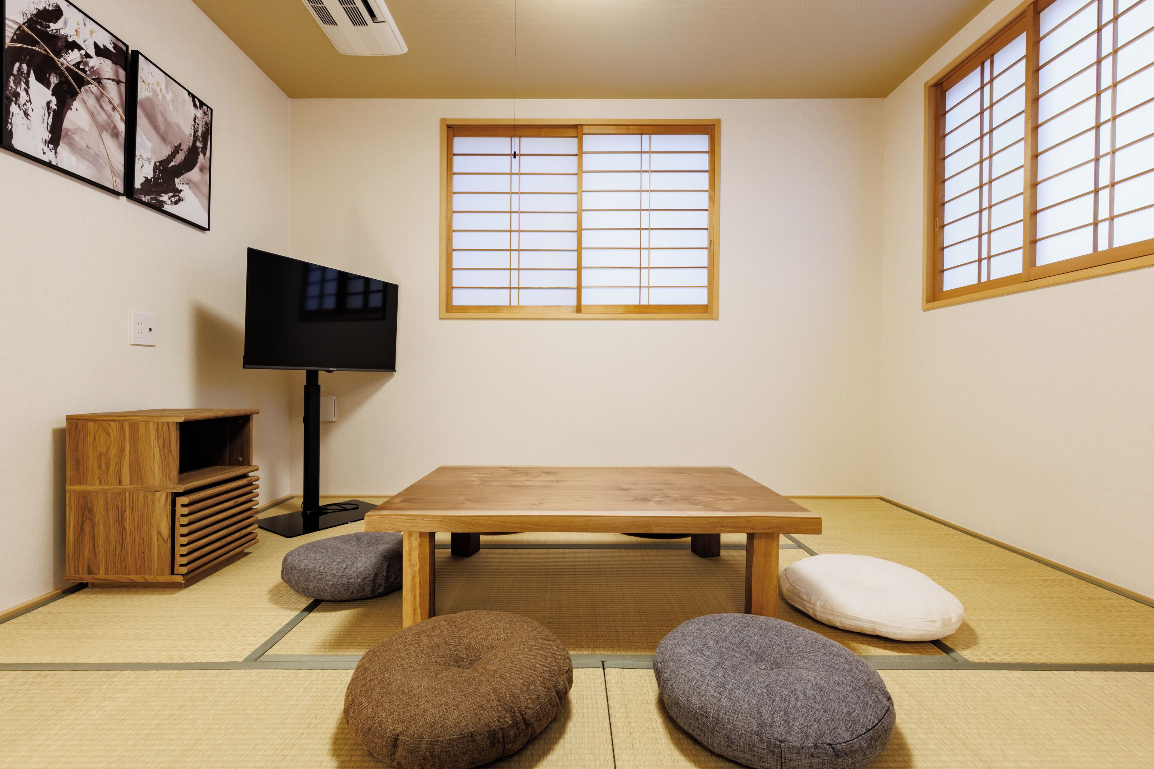 A tatami mat room with a wooden table, tatami cushions, a television, and a shoji screen window.