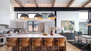 A modern kitchen with a large island, bar stools, pendant lighting, and artwork on the walls. - Luxury 4 bd home on Rollingstone Ranch Golf Course (Steamboat Springs)