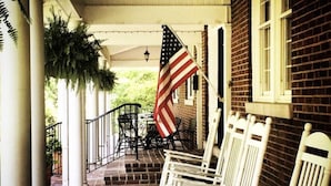 A porch with white rocking chairs, a brick building, and an American flag. - Fresh & Welcoming in the Rolling Kentucky Hills (Versailles)