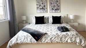 A bedroom with a large bed, two nightstands, a window with curtains, and two floral paintings on the wall. - 4 BR Spacious Home in Barrie (Barrie)