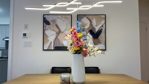 A dining area with a wooden table, a vase with flowers, abstract paintings on the wall, and modern lighting. - 4 BR Spacious Home in Barrie (Barrie)