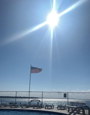 A sunny day at a waterfront with an American flag, a pool, and a bench area. - Stunning sunsets on the bay!! 1 block to the beach & next to the Convention Ctr (Ocean City)