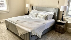 A neatly made bed with a grey headboard, two bedside tables with lamps, and a carpeted floor. - History & Hospitality at the Woodford Inn (Versailles)