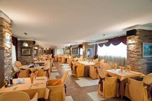 Une salle à manger d’hôtel avec de nombreuses tables et chaises, des murs en pierre et des œuvres d’art accrochées aux murs.