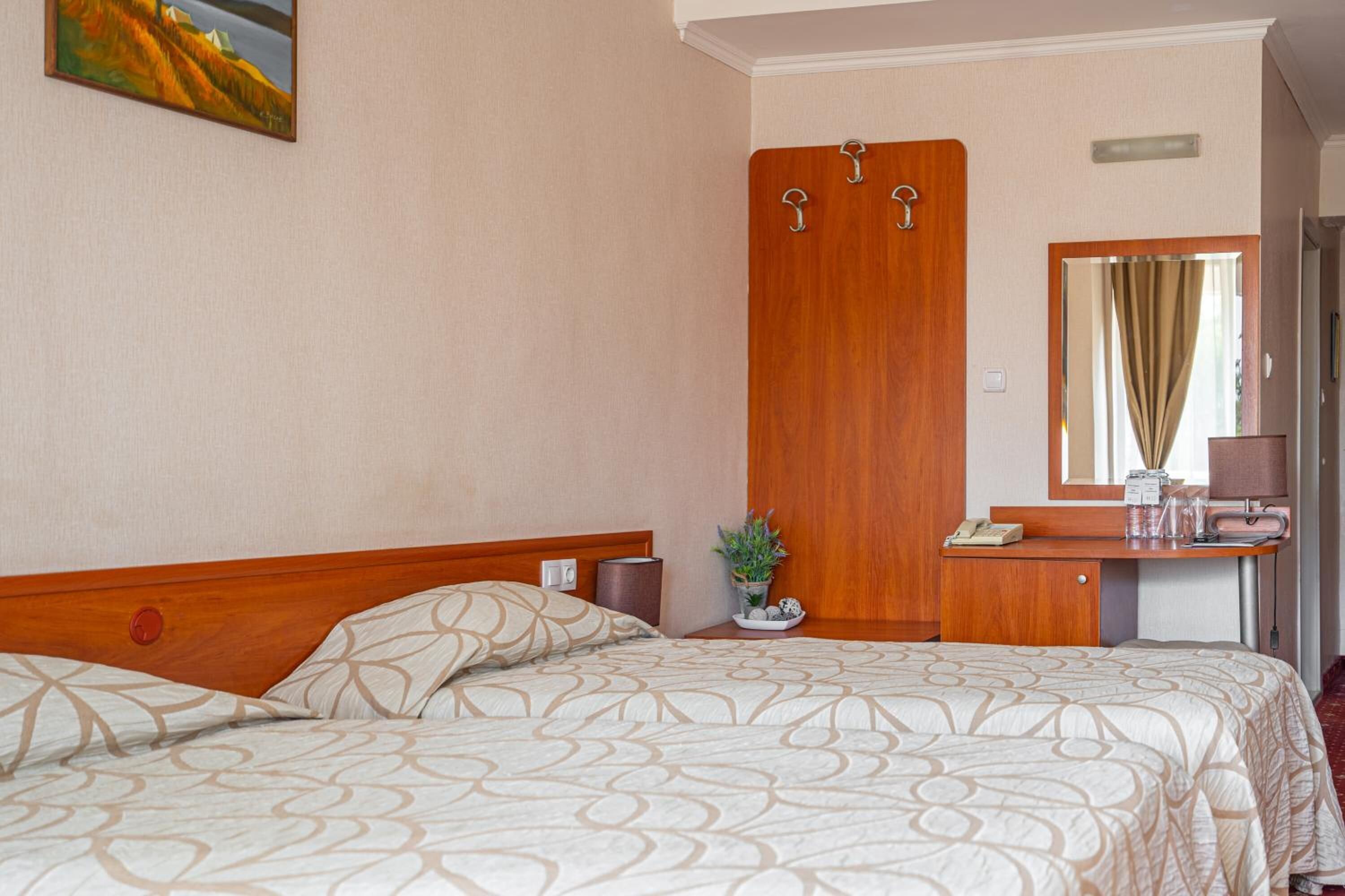 Een hotelkamer met een bed, een houten garderobe, een spiegel, een nachtkastje en een kleine potplant.