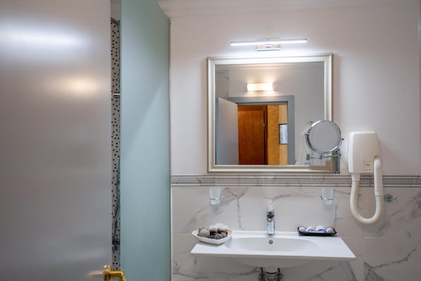 A bathroom with a white sink, a mirror, a handheld showerhead, and a towel rack.