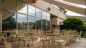 An outdoor patio with ornate white chairs and tables, large windows, and a brick wall. - Spa Hotel Hissar (Hisarja)