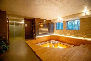 Une salle de spa moderne avec un plancher en bois, une zone de plancher chauffée, un téléviseur fixé au mur et une fenêtre donnant sur les arbres.