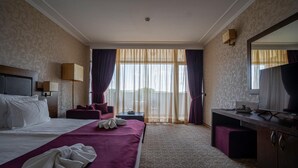 A hotel room with a large bed, a desk, a chair, a television, and a window with curtains.