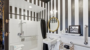 A bathroom with a shower, sink, and a vanity mirror.