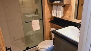 A compact bathroom with a glass shower enclosure, a white toilet, and a sink.