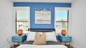 Ein Schlafzimmer mit einem Bett, zwei Nachttischen, einer blauen Wand und Blick auf die Stadt durch die Fenster.
