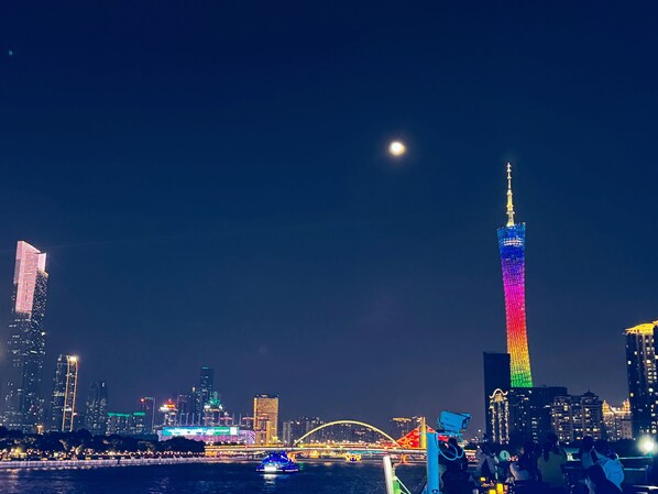Un horizonte urbano nocturno con edificios iluminados, una torre destacada y un puente.
