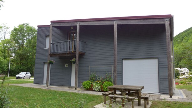 A two-story building with a balcony, a garage, and a small garden area with a wooden bench. - PASSIFLORE - Froncles (Froncles)