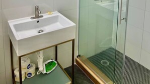 A bathroom with a white sink, a mirror, and a glass-enclosed shower. - Boutique Hotel | Double Queen | Game Day (Starkville)