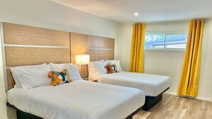 A hotel room with two beds, a headboard, a bedside lamp, and yellow curtains. - Boutique Hotel | Double Queen | Game Day (Starkville)