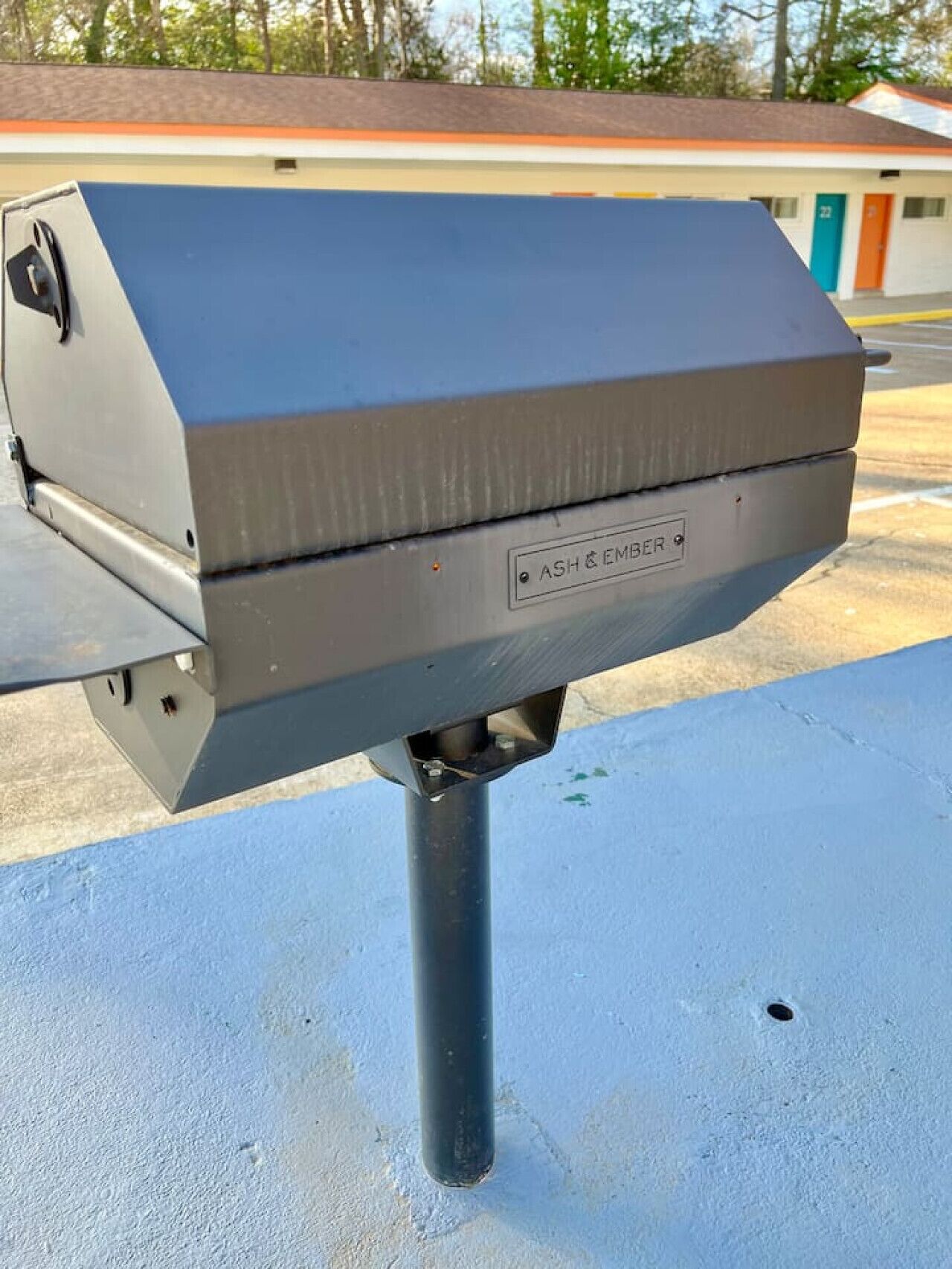 A grill with the label "ASH & EMBER" on a metal pole.