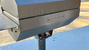 A grill with the label "ASH & EMBER" on a metal pole.