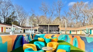 A colorful outdoor seating area with a pool, surrounded by a building with a unique mural design. - Boutique Hotel | Double Queen | Game Day (Starkville)