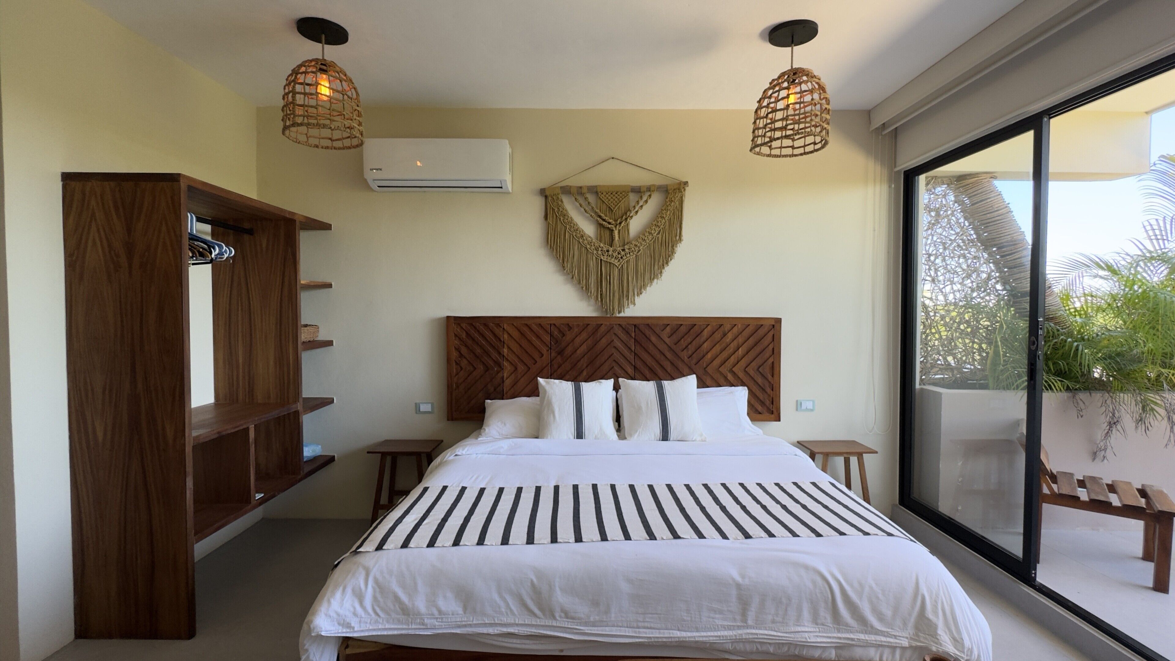 Ein Schlafzimmer mit einem Bett, einem Holz-Kopfstück, Wanddekoration aus Makramee und einem großen Fenster mit Blick.