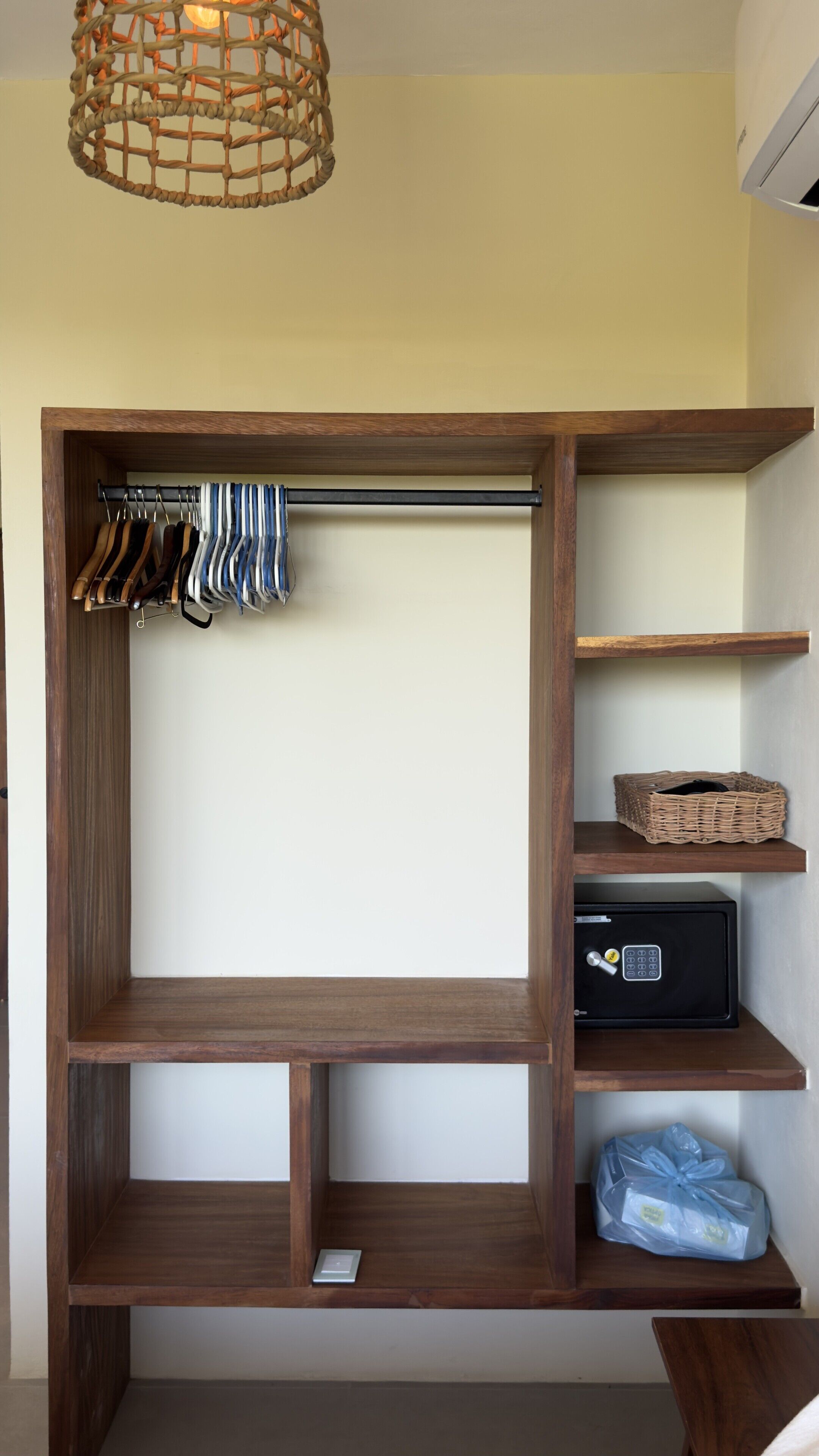 A wooden wardrobe with multiple shelves, a hanging rod, and a small safe.