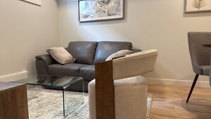 A modern living room with a leather sofa, a glass coffee table, and a grey armchair. - Cozy  Nook (Saskatoon)