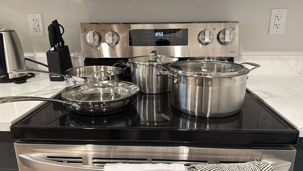 A kitchen with a stove, pots, and a digital clock. - Cozy  Nook (Saskatoon)