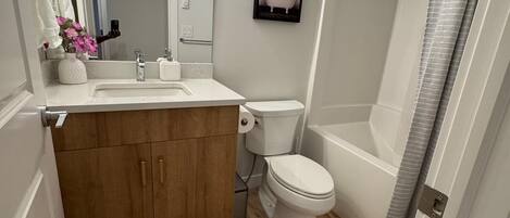 Un baño con tocador de madera, inodoro, bañera y cortina de ducha.