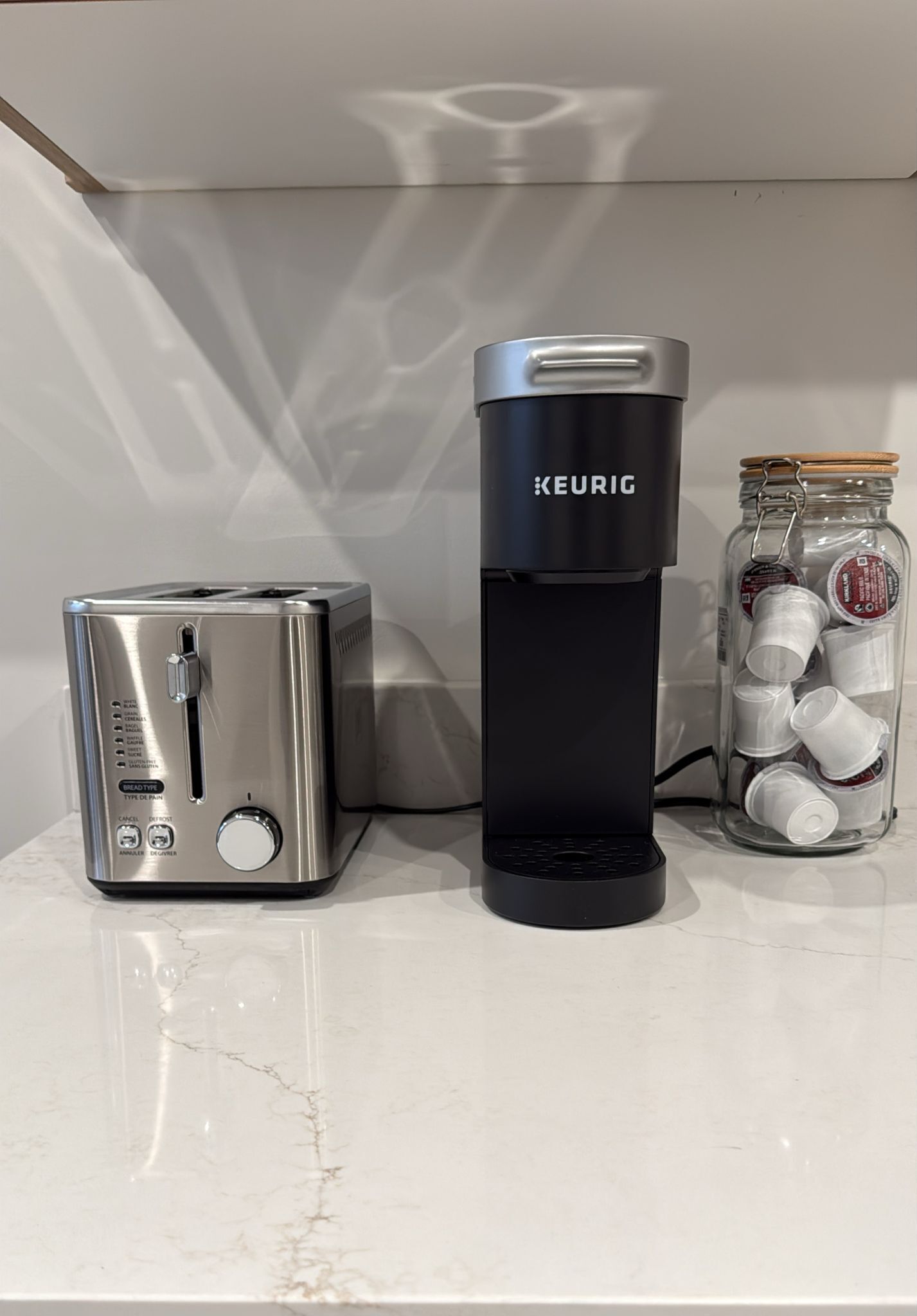 Een roestvrijstalen toaster en een zwarte Keurig koffiezetapparaat op een marmeren aanrecht.