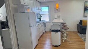 Eine moderne Küche mit weißen Schränken, einer eingebauten Mikrowelle und einem Edelstahlkühlschrank. Ein kleiner Essbereich mit Tisch und Stühlen sowie ein Fenster mit Blick ins Freie.